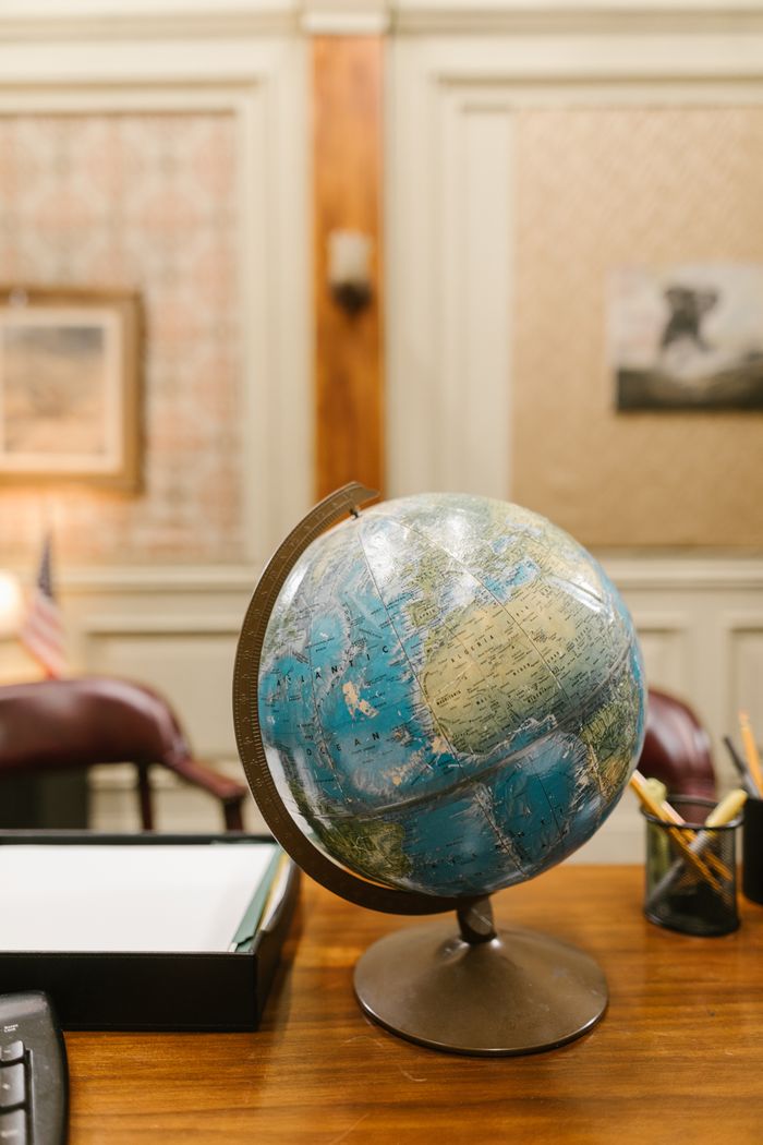 A classic globe stands on a wooden desk, surrounded by office decor and warm lighting.